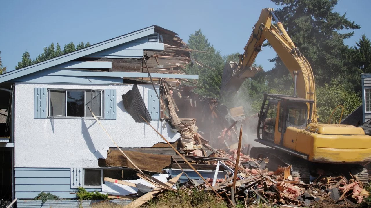 Excavator demolishing concrete structure with debris and safety barriers